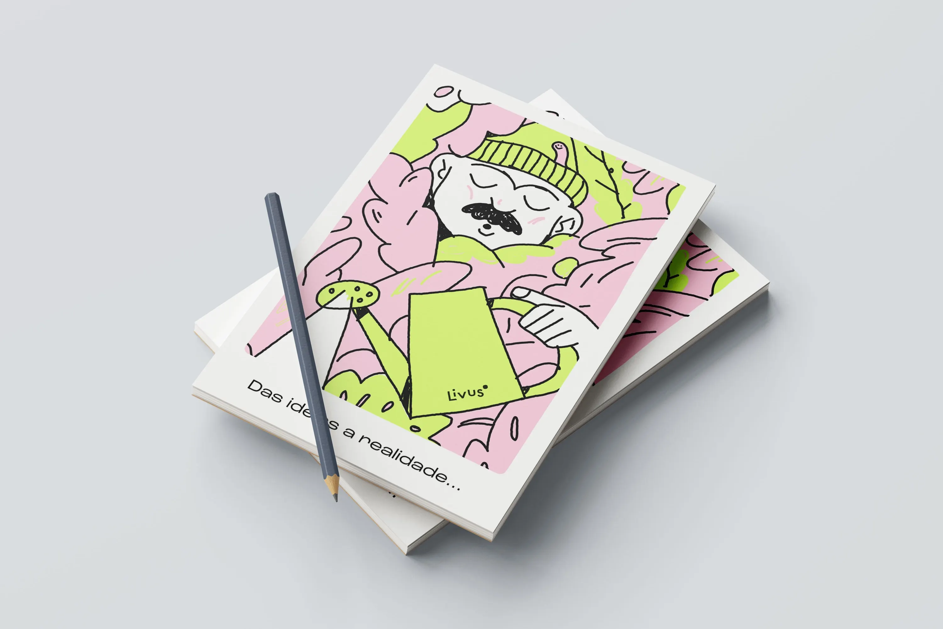 Two stacked Livus notebooks with a pencil on top, the cover illustrated in pink and lime with a man holding a watering can, captioned "Das ideias a realidade…".