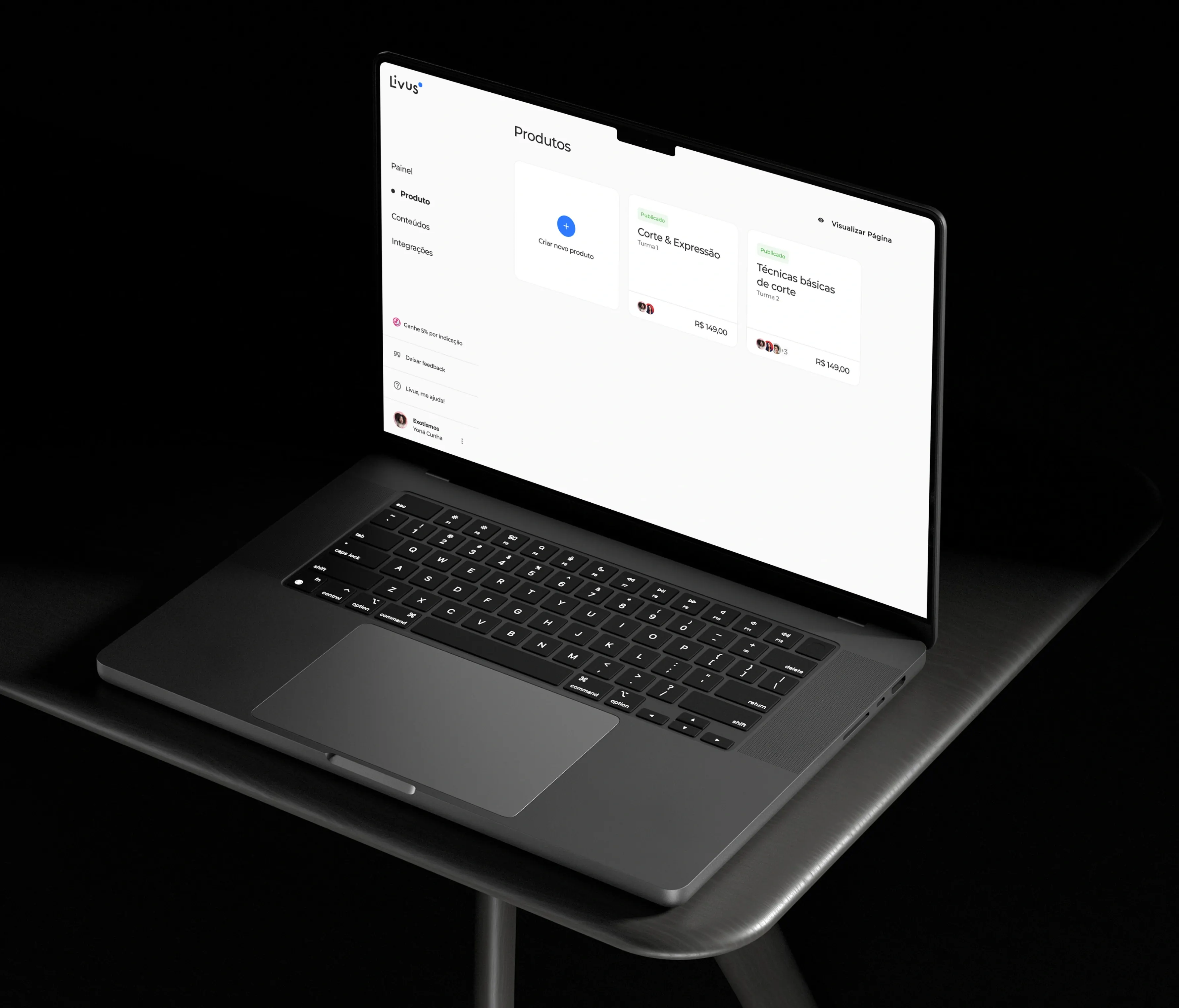 A laptop on a dark table showing the Livus "Produtos" page, with a card to create a new product beside two published courses, "Corte & Expressão" and "Técnicas básicas de corte".